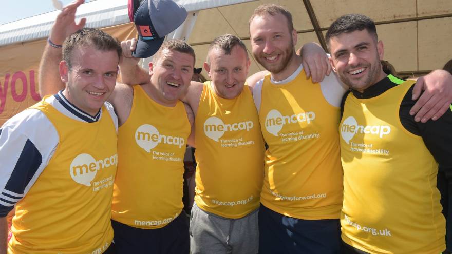 Group of 5 men posing together outside wearing yellow Mencap running vests.