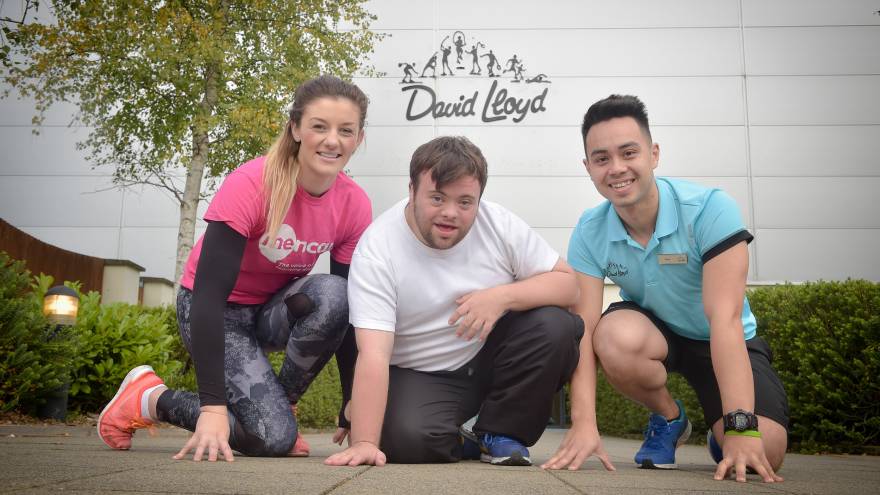 Three people in sportswear kneeling in front of a David Lloyd sports centre