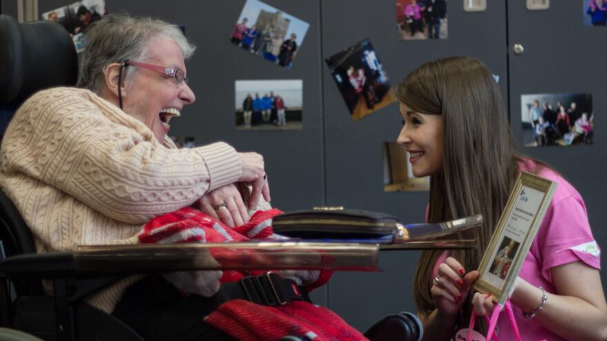 Two people laughing together in front of wall of photographs