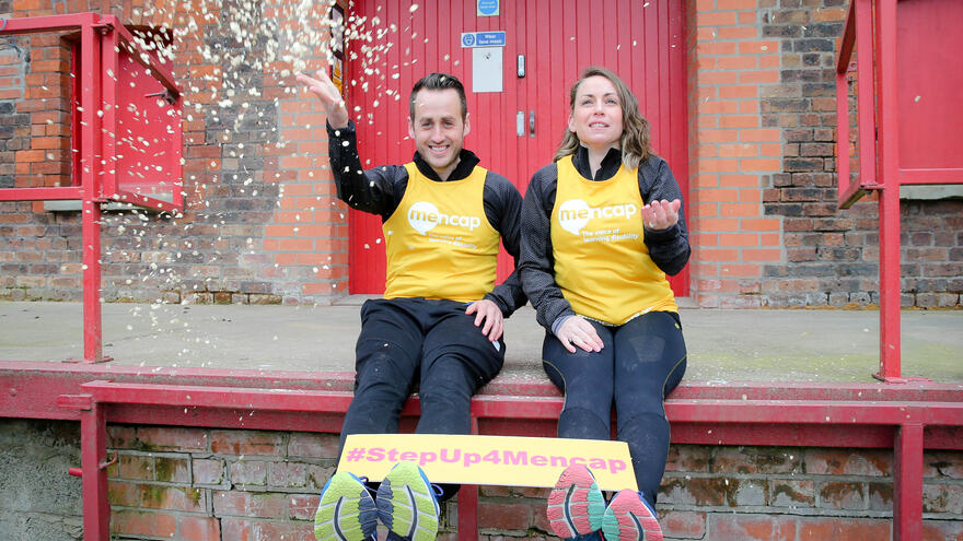 Two people outside holding a #StepUp4Mencap banner