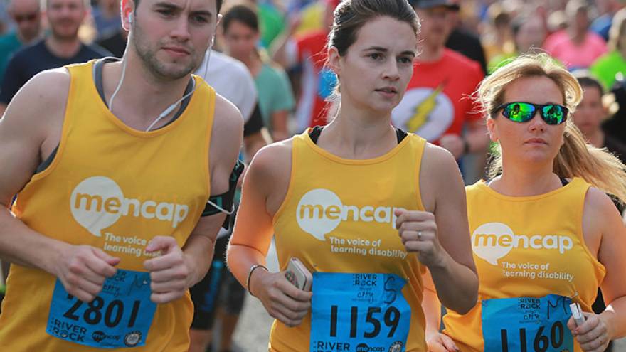 Three people running in race wearing Mencap running vests.