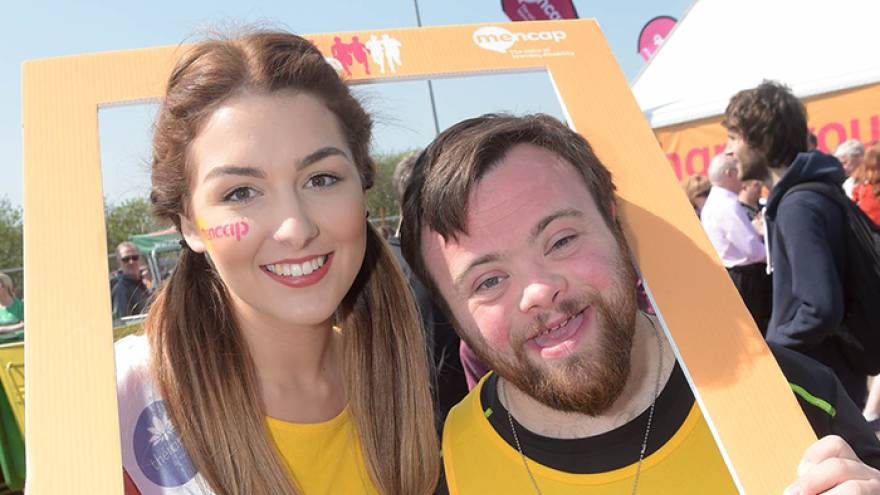 Man and woman stood together smiling with Mencap frame around their heads.