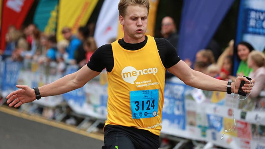 Young man running wearing Mencap running vest crossing finishing line of race.