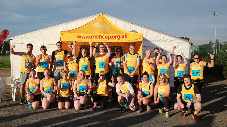 Group of people wearing Mencap running bests cheering.