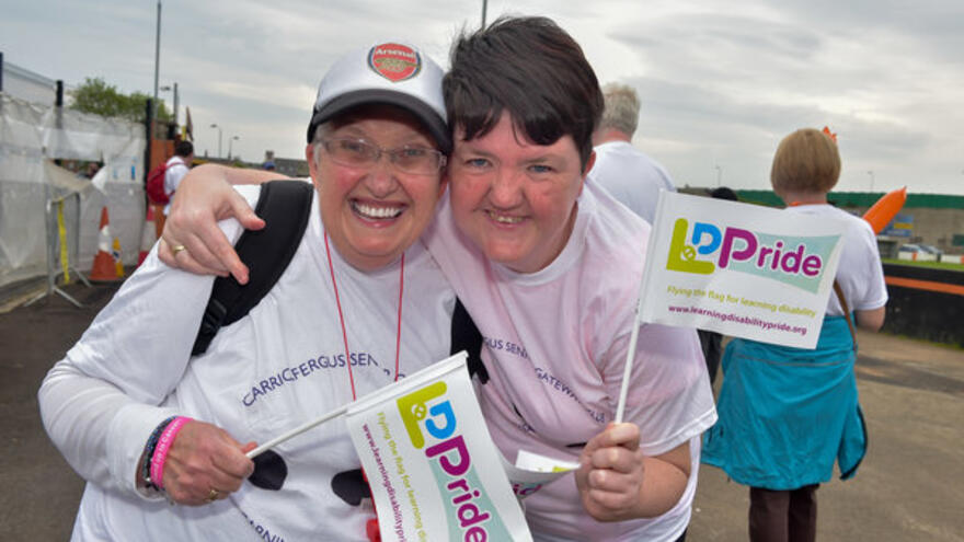 Two people with arms around each other holding LD Pride flags, smiling at camera