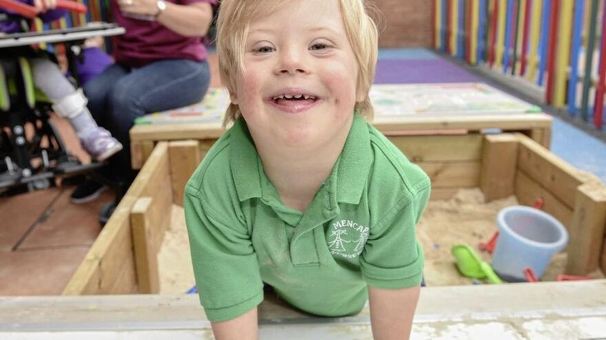 Young boy with blonde hair and green top smiling at the camera
