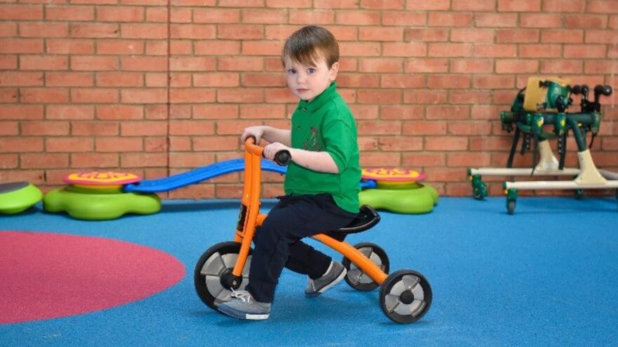 Young boy playing on an orange bicycle