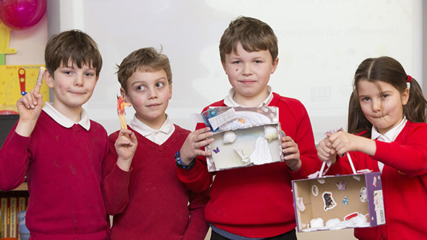 Children in classroom holding art projects they have made.