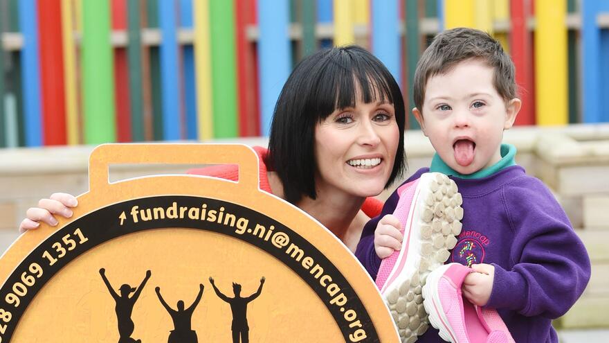 Woman and young boy stood outside next to MoveIt4Mencap sign