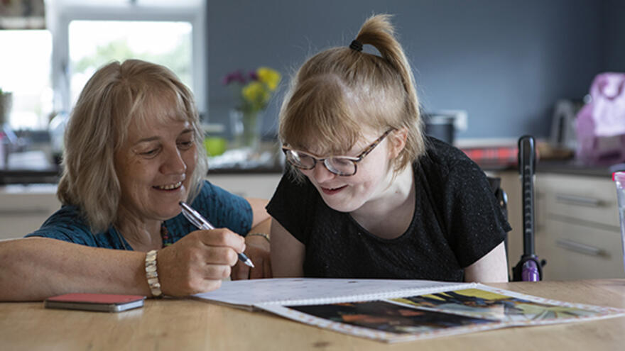 Woman helping young person with paperwork sat at kitchen table