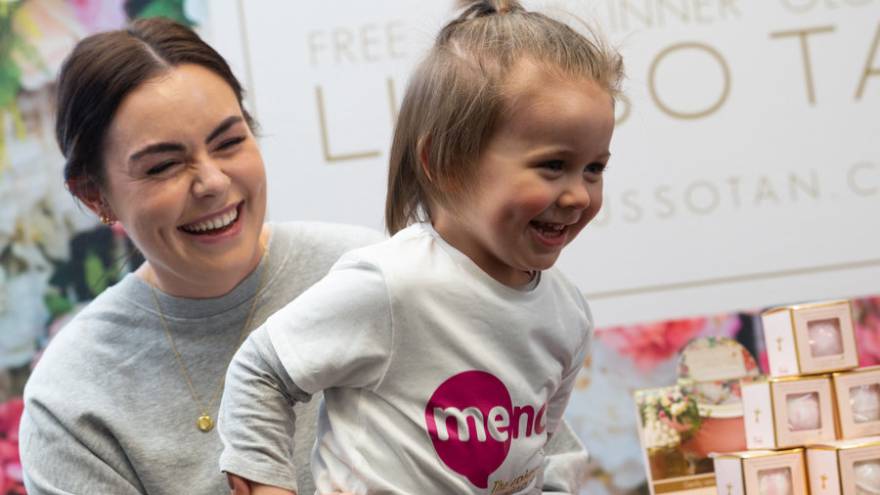 Woman laughing holding on to a young child who is also laughing and wearing a Mencap t-shirt.