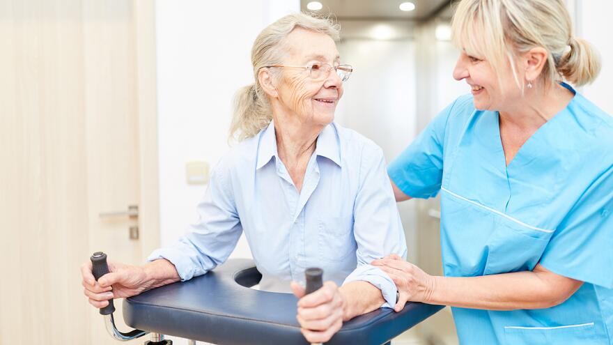 A woman in a walking frame being helped by a nurse