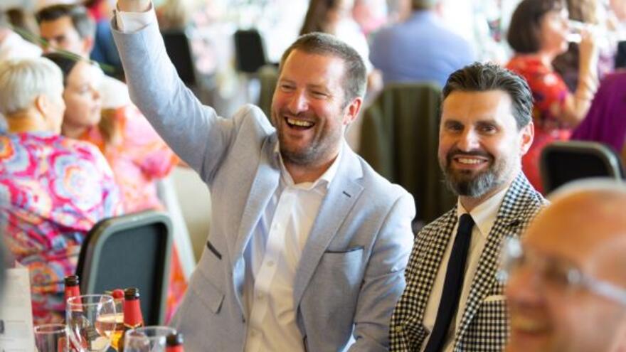 A corporate fundraising event with people sitting at tables with their hands raised