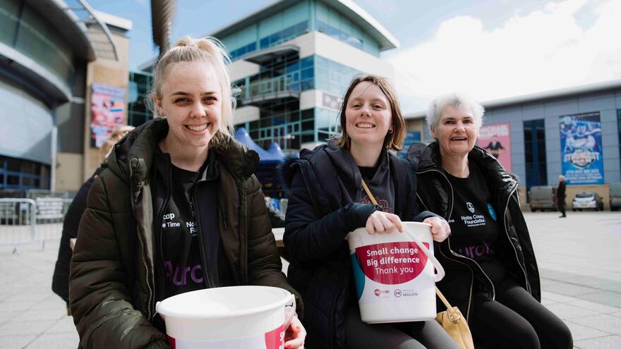 Three fundraisers are sitting on a bench holding Mencap collection buckets