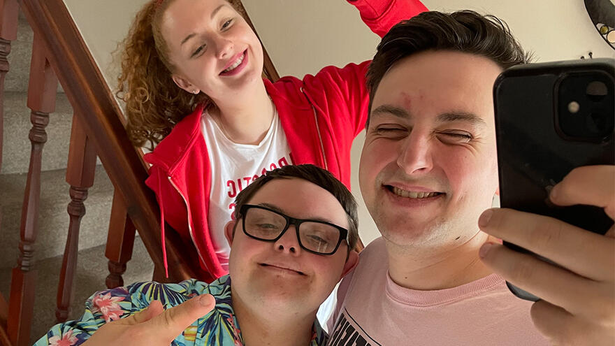 Three people standing indoors around stairs taking a selfie