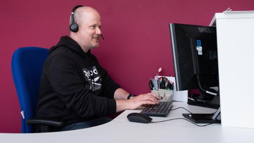 Man sitting at computer wearing a telephone headset 
