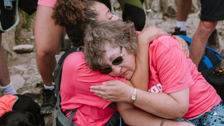 Two women sitting on a rock embracing one another wearing Mencap t-shirts 