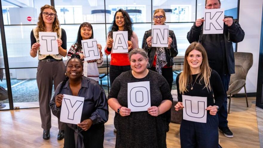 Eight people holding up letters that spell Thank You