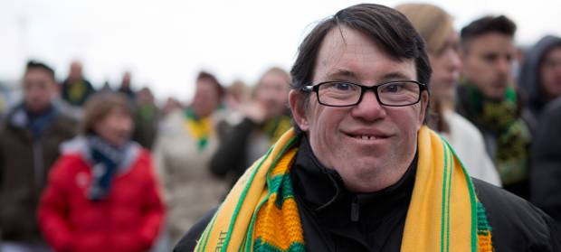 Man stood in crown wearing yellow and green football scarf