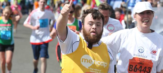 Man in Mencap vest taking part in running event, waving his arm in the air.
