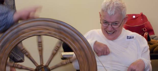 Person in white top, smiling whilst using a spinning wheel