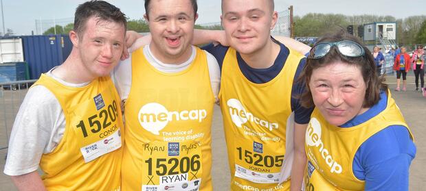 Group of four people stood outside wearing yellow Mencap running vests