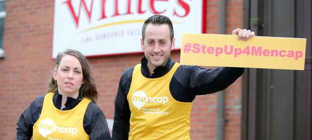 Two people stood outside holding a #StepUp4Mencap banner