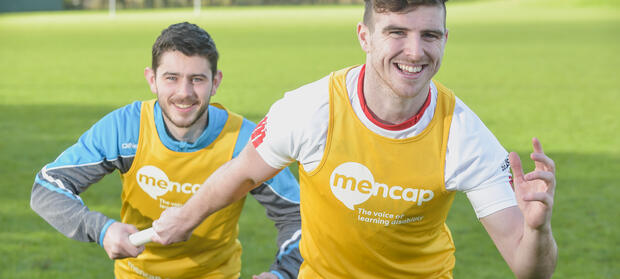 Two young men in Mencap running vests passing a relay baton