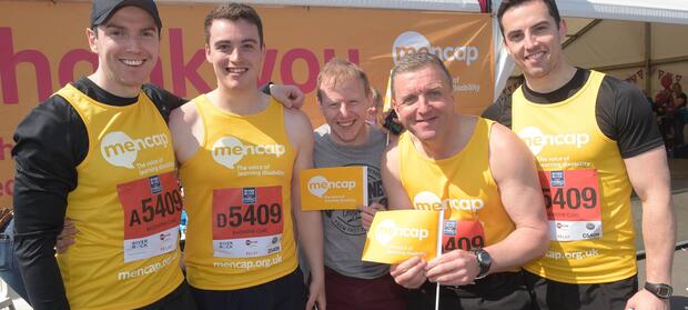 Group of men outside wearing yellow Mencap running vests and holding Mencap flags