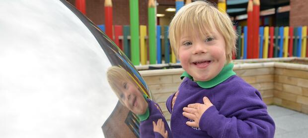 Young boy with blonde hair and purple jumper stood next to large silver dome, smiling at the camera