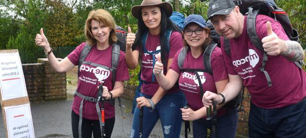 Group of people wearing hiking gear and Mencap t-shirts giving thumbs up signs to the camera whilst stood outdoors