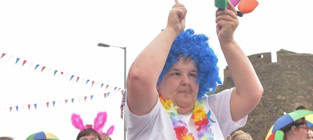 Person wearing bright blue wig waving their hands above their head, taking part in a parade.