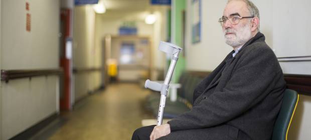 Older gentleman holding crutches sat on a chair in a hospital waiting room