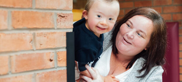 Woman with long dark hair holding young boy next to a brick wall.