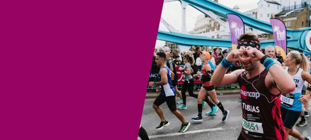 A  man making a heart shape with his hands whilst running past the camera in a marathon race