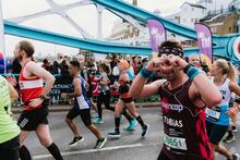 A  man making a heart shape with his hands whilst running past the camera in a marathon race